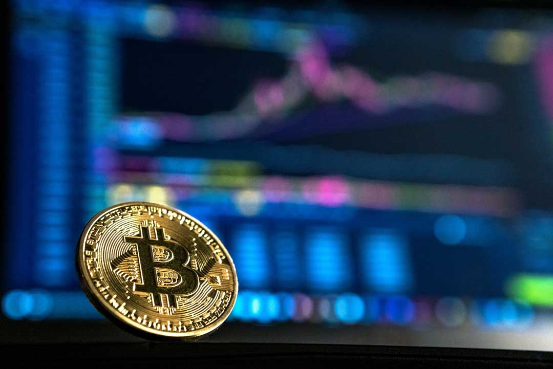 Bitcoin (BTC) is illustrated as a physical gold coin with some colorful charts in the background