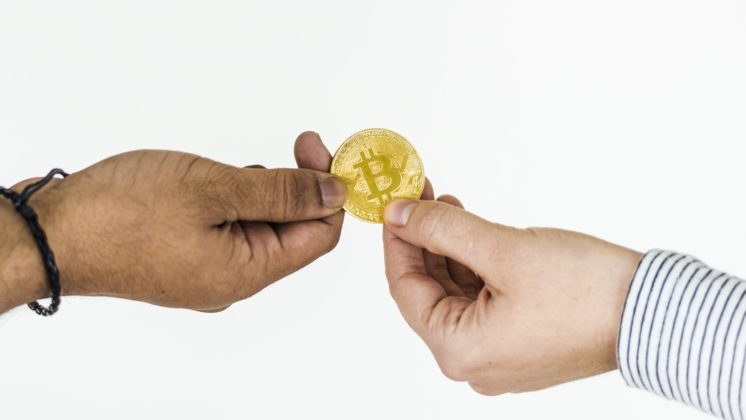 two people holding a bitcoin coin with a white background in NZ