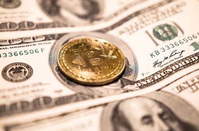 A gold bitcoin placed on the center of a one hundred dollar bill