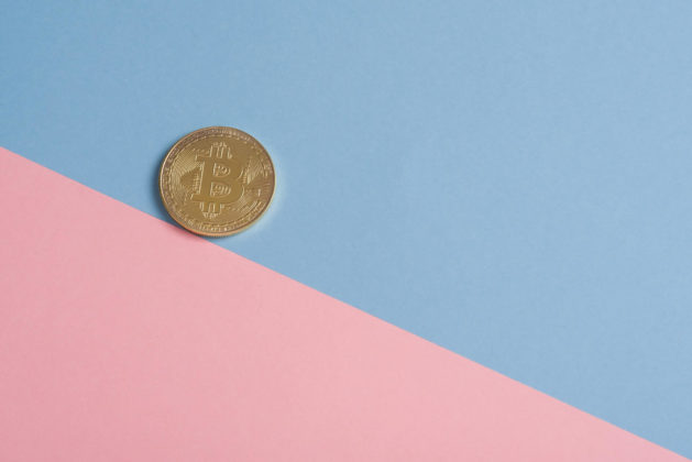 Image of a golden bitcoin backdropped in a two tone pastel colored background at an angle