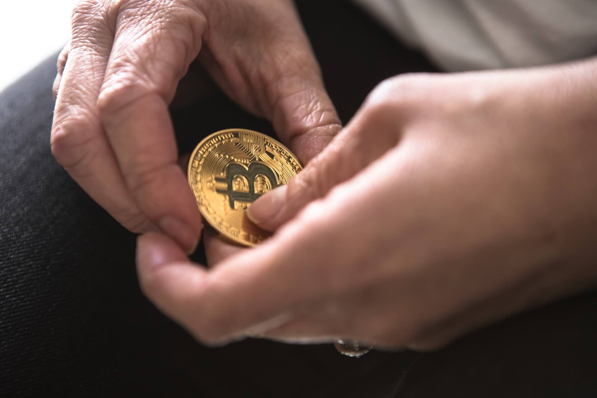 Photo of a man holding a golden bitcoin between his two fingers to depict what are stablecoins.