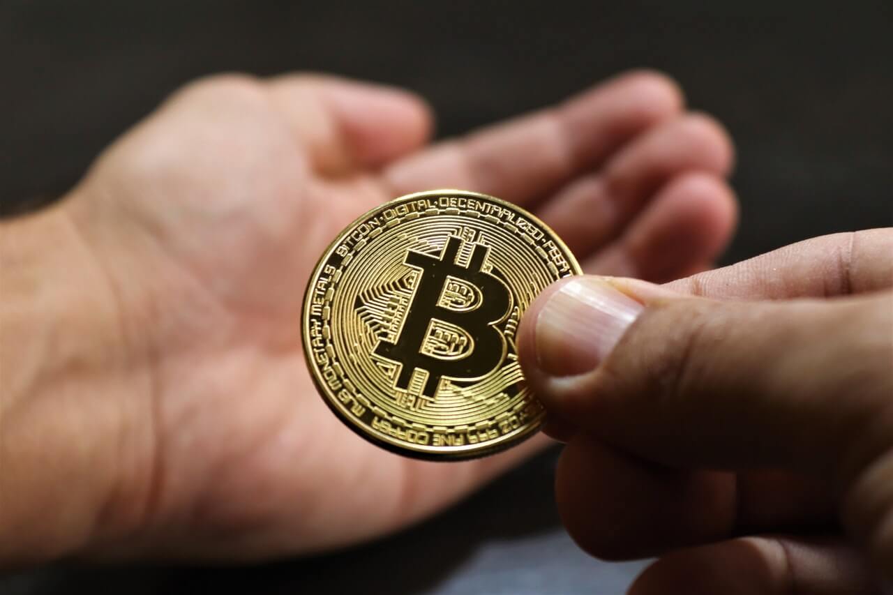 A golden bitcoin being held by a man's hand about to be given to another person