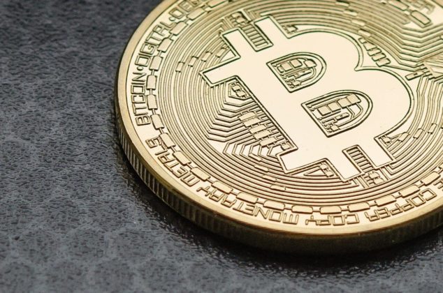 Picture of a golden bitcoin backdropped on a dark gray surface.