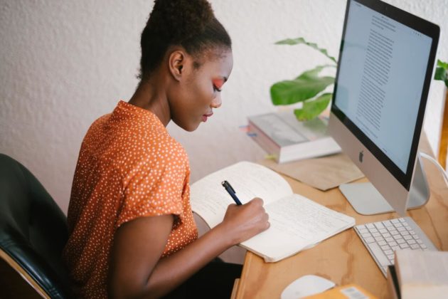 Image of Nigerian woman sitting in front of a desk with an imac computer writing notes on a piece of paper