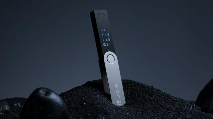 Ledger Nano X vertically placed on a pile of black sand with keylighting from above