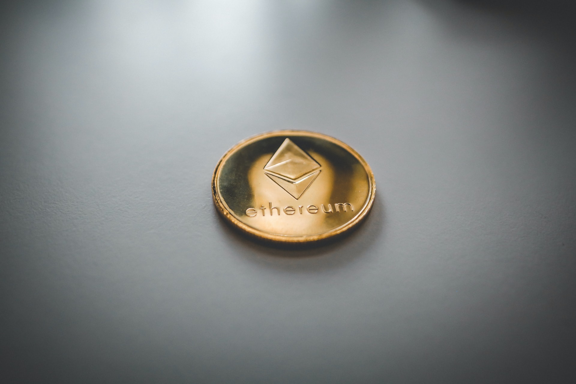 A physical ethereum coin on a gray background. 