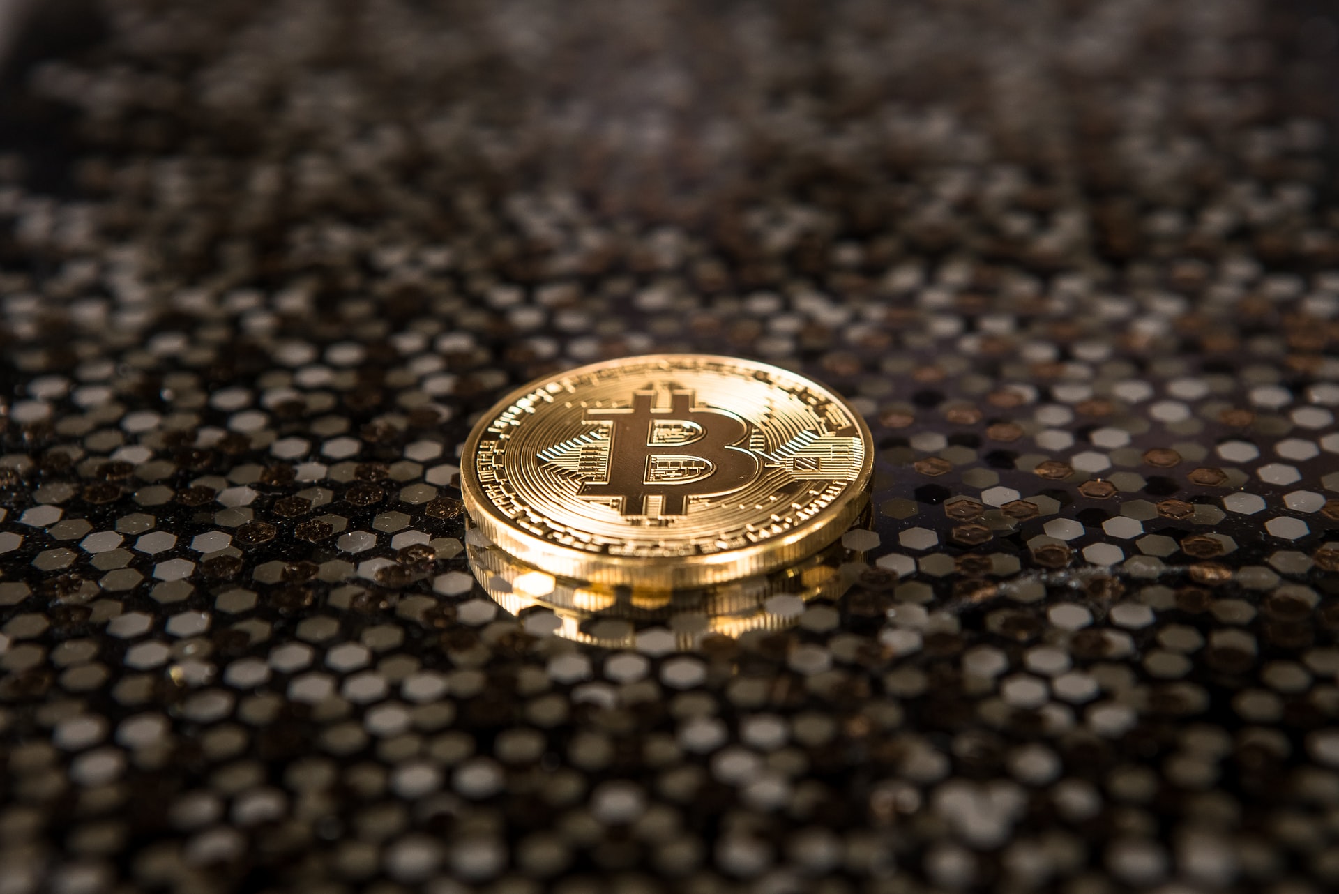 Photo of a physical bitcoin on top of a dark clear table. 