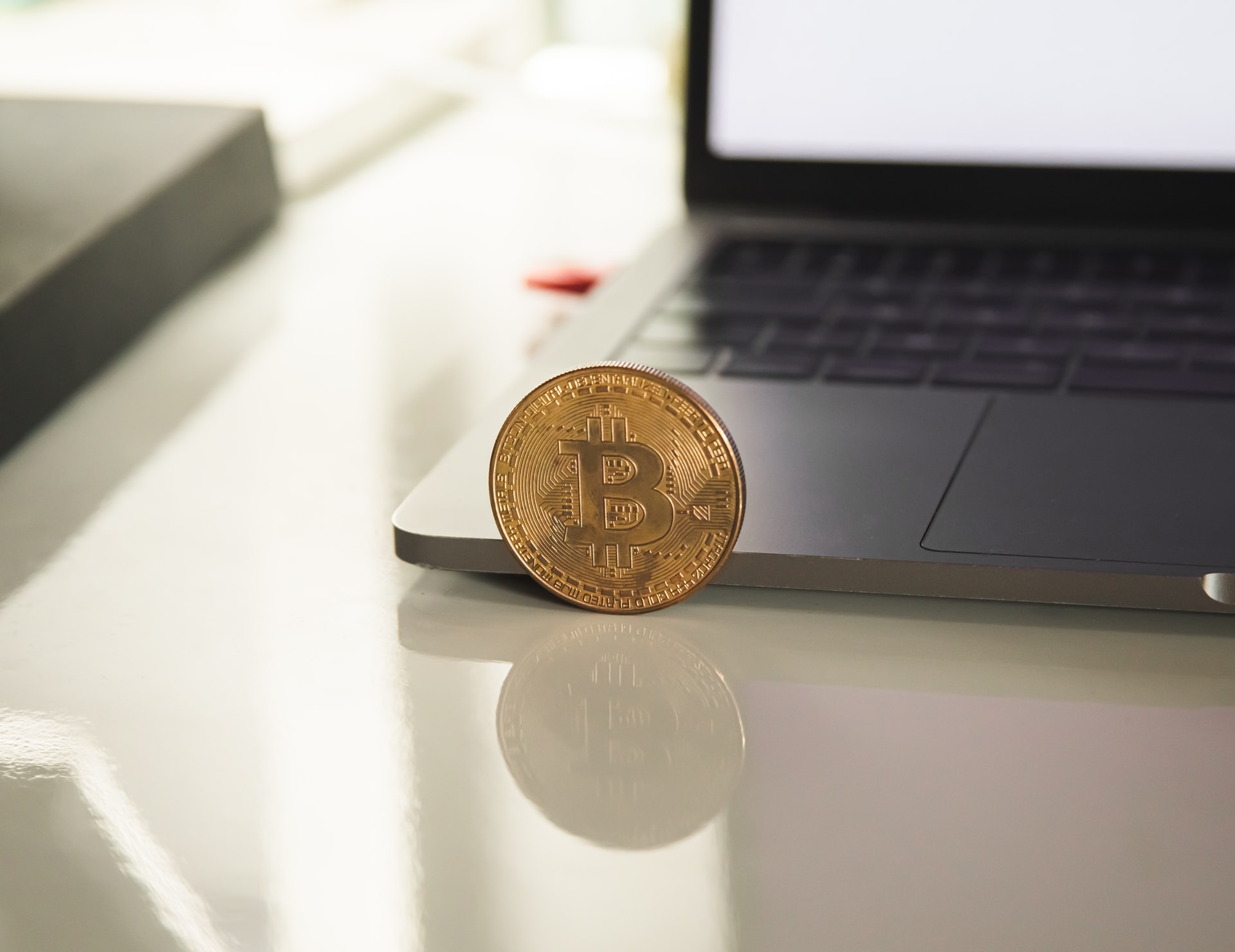 Image of a physical bitcoin next to a macbook laptop to depict the topic of what is proof of stake.