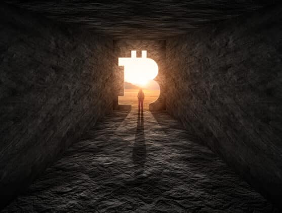 Photo of man standing over a cave entrance in a shape of Bitcoin.