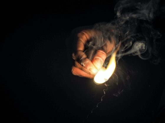 Illustration of a man holding a flaming match to illustrate the idea of crypto coin burns.