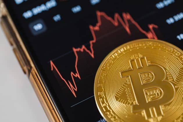 Image of a bitcoin on top of a phone displaying a graph