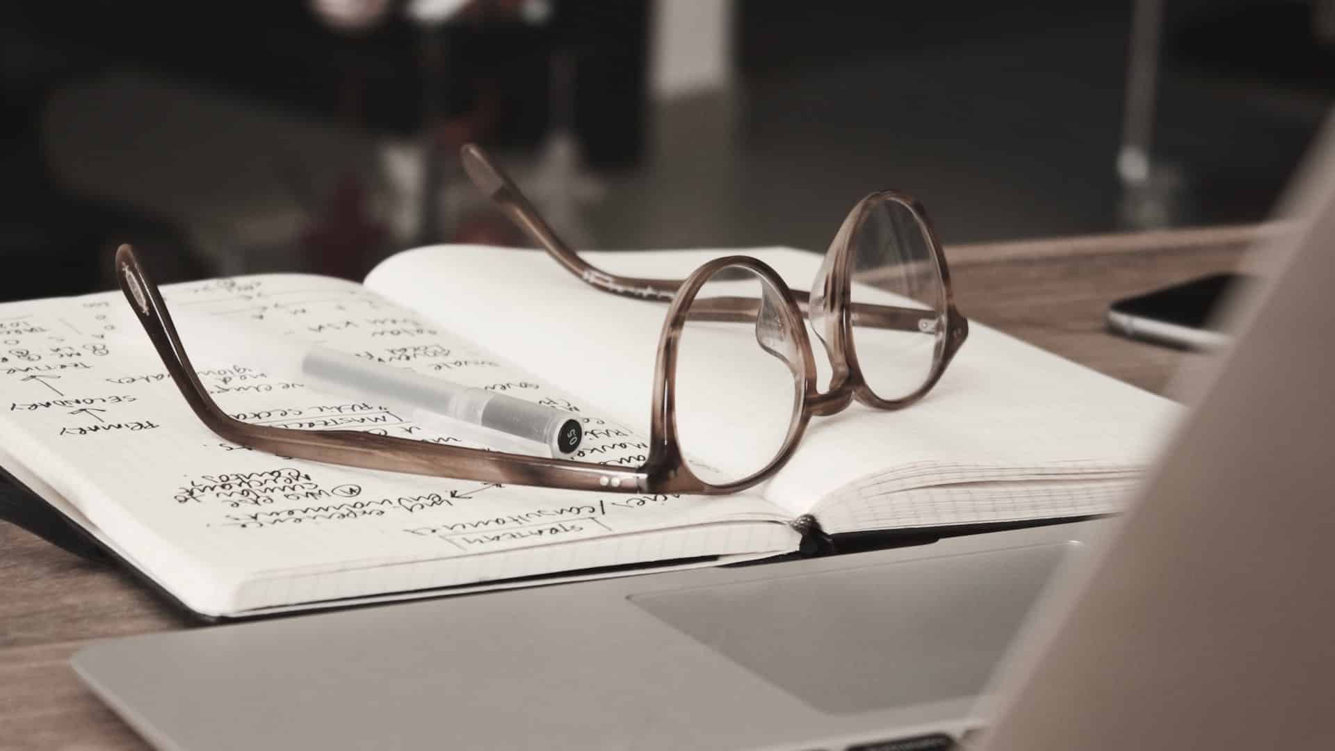 A pair of glasses that sit atop of an open book.