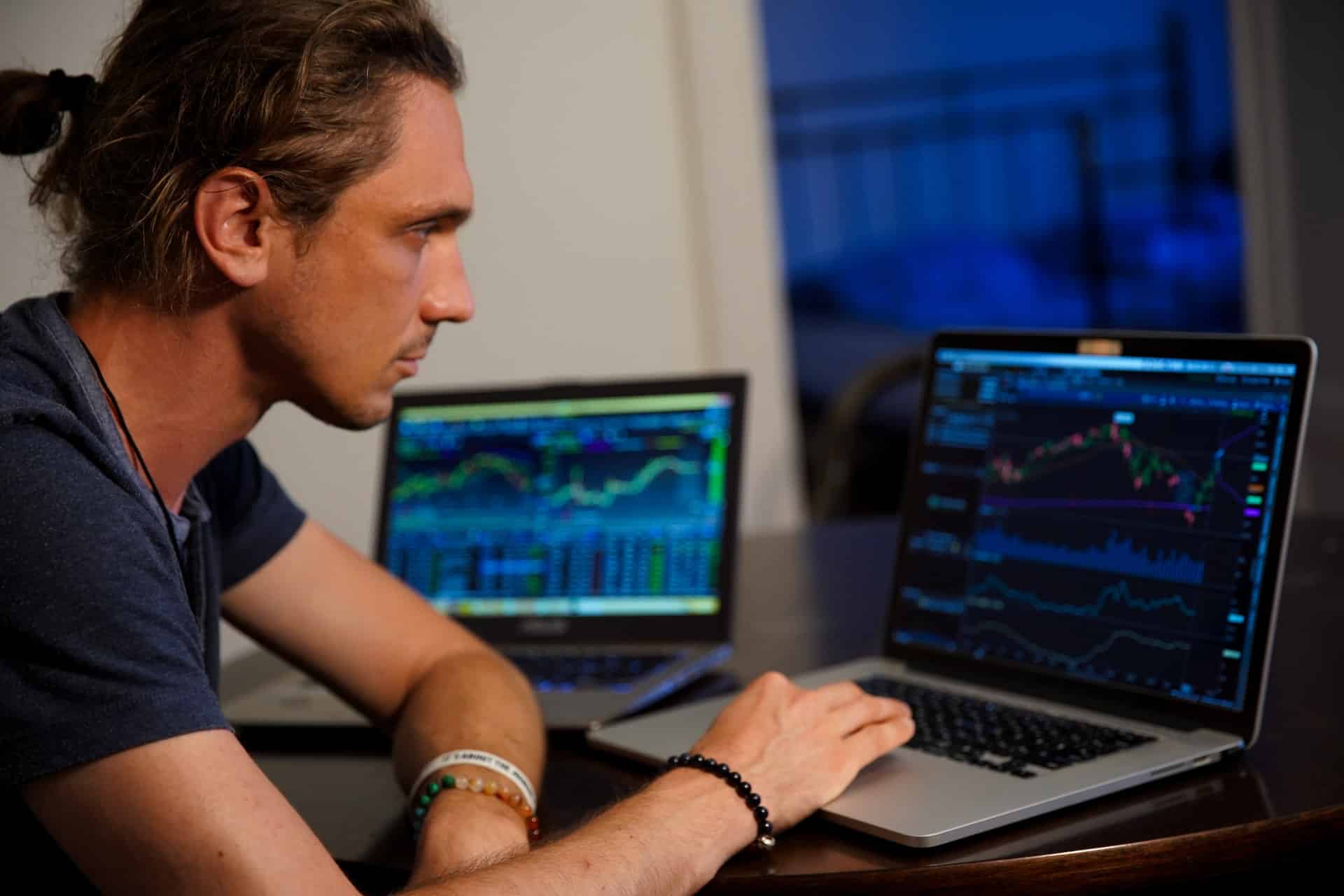 A man with two laptops open and trading cryptocurrency.